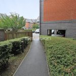 Pathway between hedges leading to residential buildings.