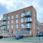 Modern brick building with balconies and parked cars.