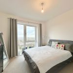 Bright bedroom with bed, mirror, and window view.