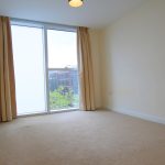Empty room with large window and cream carpet.