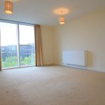 Spacious room with large window and beige carpet.