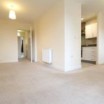 Spacious empty room with carpet and kitchen view.