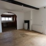 Empty room with wooden floor and arched kitchen view.