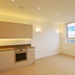 Modern kitchen with light wood flooring and large window.