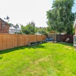 Sunny garden with wooden fence and lawn chairs.