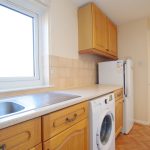 Bright kitchen with washing machine and wooden cupboards.