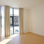 Bright empty room with large window and wooden floor.