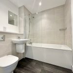 Modern bathroom with bathtub and grey tiles.