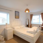Bright double bedroom with white bed and two windows.