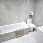 Modern grey tiled bathroom with bathtub and toilet.