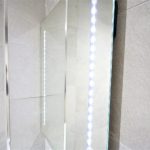 Close-up of illuminated bathroom mirror and tiles.