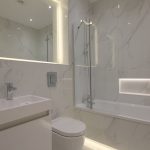 Modern bathroom with marble tiles and illuminated mirror.