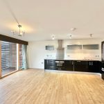 Modern kitchen with wooden floors and large windows.