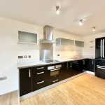 Modern kitchen with black appliances and wooden flooring.
