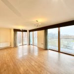 Spacious modern apartment with large windows and wood flooring.