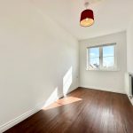 Sunlit empty room with wooden floor and window.