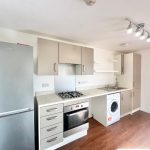 Modern white kitchen with appliances and wooden flooring.