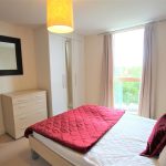 Bright bedroom with red bedding and large mirror.