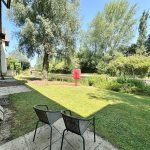 Riverside garden view with chairs and trees.