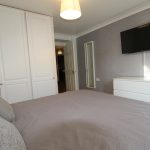 Modern bedroom with wardrobe and TV on wall.
