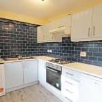 Modern kitchen with blue tiled backsplash and appliances.