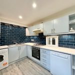 Modern kitchen with blue tiled backsplash and appliances.