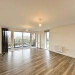 Spacious empty room with wooden flooring, large windows.