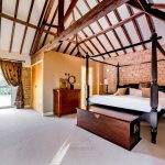 Spacious bedroom with wooden beams and stone wall.