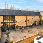 Stone barn with courtyard, trees, and parked car.