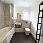 Modern bathroom with bathtub, sink, toilet and towel rack.