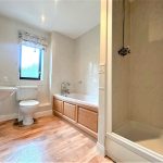 Modern bathroom with wooden flooring and white fixtures.