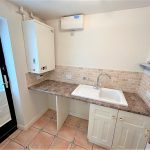 Small kitchen with sink, boiler, and tiled backsplash.