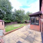 Spacious patio with garden and trees, red brick house.