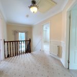 Carpeted hallway with chandelier and wooden bannister.