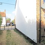 Narrow driveway with gate beside brick house.