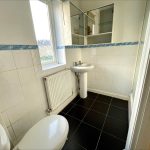 White tiled bathroom with pedestal sink and toilet.