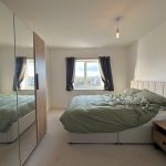 Modern bedroom with green bedspread and mirrored wardrobe.
