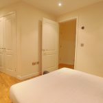 Bright double bedroom with wooden flooring and wardrobes.