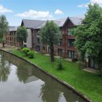 Canal-side apartments with lush greenery and moored boat.