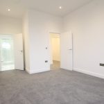 Empty white room with grey carpet and two doors.