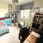 Cosy bedroom with desk, shelves, and colourful bedspread.