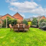 Garden with wooden table, chairs, swing chair, and bushes.