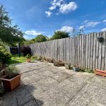 Sunny garden with patio and wooden fence.