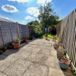 Sunlit garden with paved path and fences.