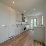Modern kitchen with wooden flooring and white cabinets.