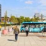 People walking alongside a moving blue bus in city.