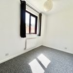 Small bright room with grey carpet and window.