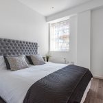 Modern bedroom with grey headboard and large mirror.