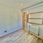 Empty room with wooden floor, shelves, and radiator.