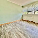 Empty room with wooden flooring and large window.